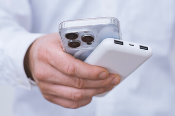 Close-up of a man holding a smartphone and a white power bank. Portable battery charger and mobile phone concept, modern technology, digital lifestyle and wireless charging.