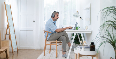 Portrait of happy caucasian business senior man casual cloths shirt work in home office desk using head phone computer. Small business employee freelance online sme marketing e-commerce telemarket