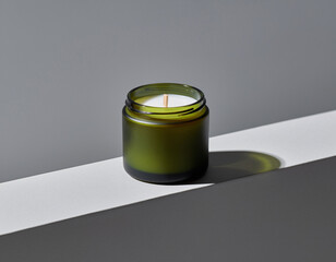 Green candle sits on white surface casting long shadow against gray wall, creating minimalist and calming atmosphere.