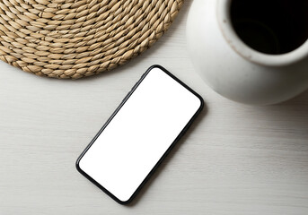 Top View of Smartphone with Blank White Screen on Textured Wooden Table with Round Woven Mat and Cream Ceramic Vase Mockup