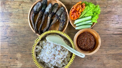 Authentic Indonesian meal featuring rice, fried fish, sambal, cucumber, tomato, and lettuce served on rustic wooden table. Perfect image for culinary, culture, and traditional lifestyle concepts.