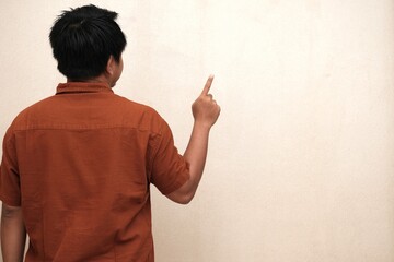 Southeast Asian man in a brown shirt seen from behind, raising one finger and pointing upward,...
