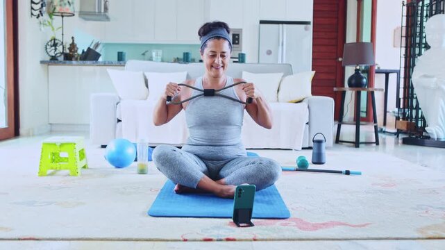 Woman exercising with resistance band during online fitness class at home