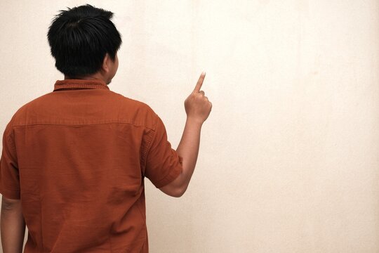 Southeast Asian man in a brown shirt seen from behind, raising one finger and pointing upward, suggesting an idea or direction.