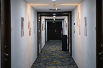 Long, empty hotel corridor with carpeted floor, closed doors on both sides, and soft ceiling lighting creating a quiet atmosphere.

