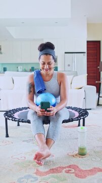 Fit woman smiling and using smartphone after home workout