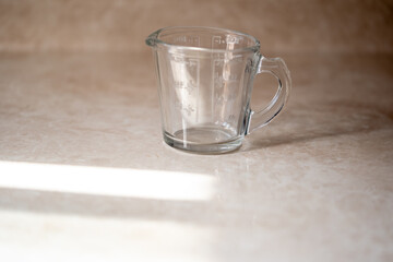 taza medidora de vidrio con asa vacía, posada sobre encimera de la cocina con luz del sol