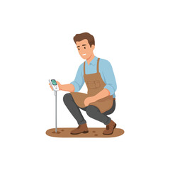 A male gardener in a brown apron crouching to test the soil with a digital meter probe.