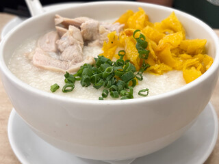 A close-up shot of a steaming bowl of traditional Asian congee (rice porridge), served in a white ceramic bowl.