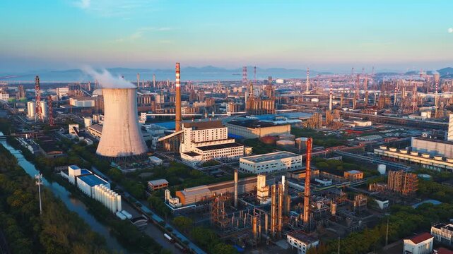 Aerial shot of a massive oil refinery and chemical plant industrial complex with a cooling tower emitting steam at golden sunset light