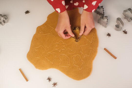 An overhead view of the hands of a young woman making gingerbread by cutting out cookie shapes from the dough. Christmas sweets made from ginger dough.