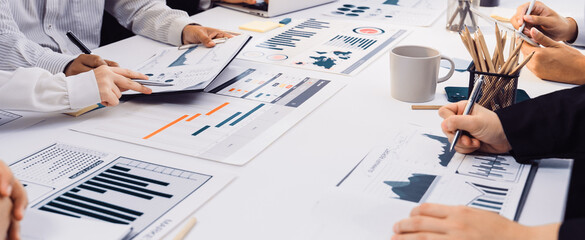 A group of diverse professionals engaged in a business meeting, analyzing graphs and charts on a white table, highlighting teamwork and strategic planning in a modern office. SACTR