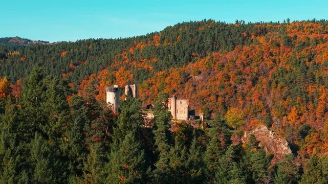 Aerial shot revealing the castle of Rochebaron behind a tree line on a sunny day during fall season in Haute Loire departement, Auveergne Rhone Alpes region, France