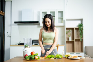 Fit woman preparing fresh salad with vegetables on wooden cutting board in kitchen. Concept of healthy food, clean eating, and fitness lifestyle.