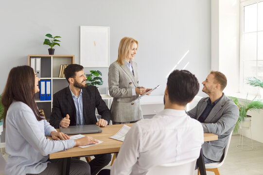 Positive businesswoman delivers presentation or meeting to team of colleagues in office, group work and conversation, highlighting people and teamwork in a collaborative atmosphere.