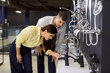 Couple examines faucets in plumbing store showroom. Clients check design and quality of chrome...