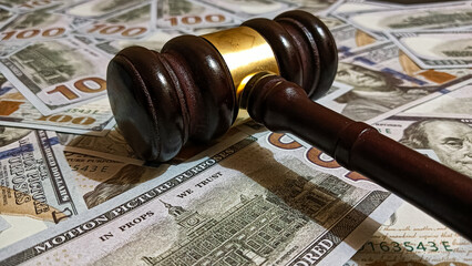 Wooden judge gavel placed on a pile of hundred-dollar bills representing law, justice, corruption, and financial judgment in legal or business contexts.