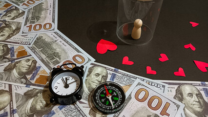 A creative composition featuring a small clock, compass, dollar bills, red paper hearts, and a wooden figure under a glass, symbolizing the connection between time, love, and financial direction.