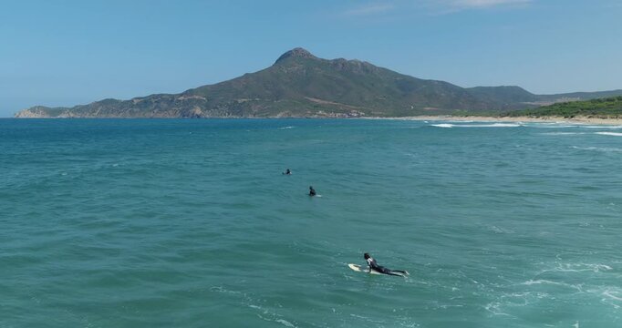 Surfers enjoy calm waters near mountainous Buggerru, Sardinia, Italy