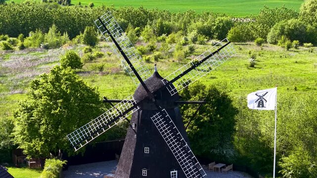 Aerial view of a historic black windmill surrounded by trees and pathways on a sunny summer day in Denmark