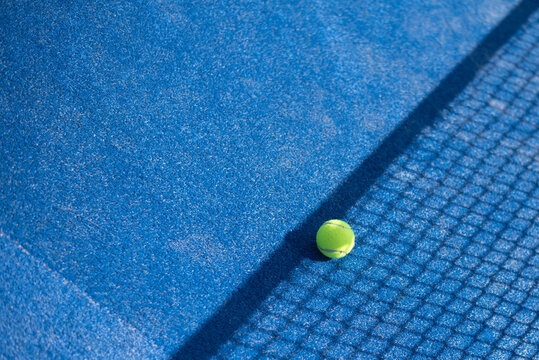 One tennis ball on blue court near net. Close up. Space for text. Active sport tennis or padel.  activity dynamic interesting game
