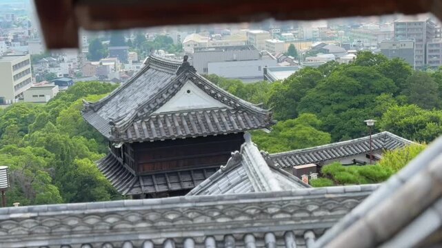 From Kochi Castle (Japan&rsquo;s Top 100 Castles, 12 original tenshu), Window View: Gray-Tiled Ancient Architecture in Lush Forest Overlooking Urban Complex.