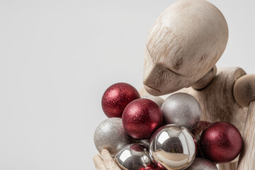 Wooden mannequin holding delicate silver and red Christmas balls, reflecting joy, unity, and warmth of holiday season, in artistic studio setup with soft shadows on white background 