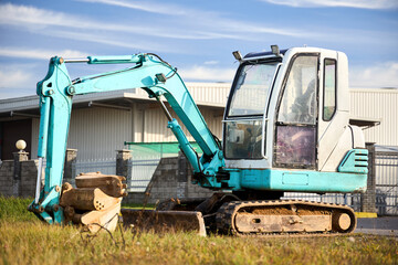 Mini excavator at construction site. Compact construction equipment for operative earthworks. Tracked green and white mini excavator digger with attachments in bucket.