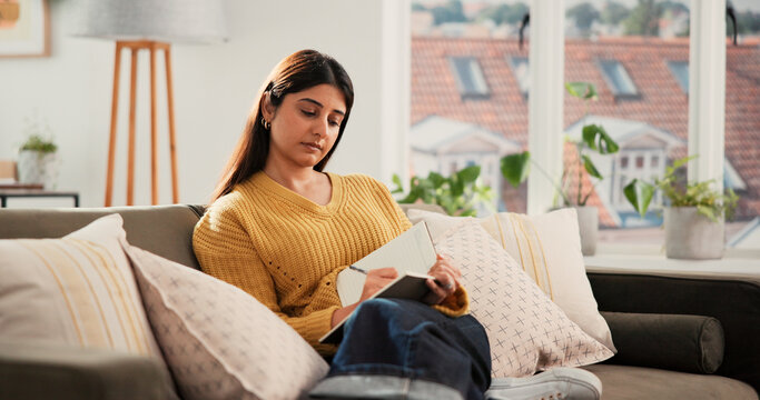 Woman, relax and writing on sofa with diary for planning goals, creative idea or process emotions. Daily reflection, notes or person in home with journal for self improvement, inspiration or insight. - Powered by Adobe