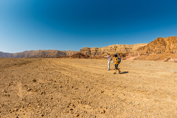 Two active backpackers stroll through the desert against a blue sky. Mother and child on a hike. Summer camp. Timna National Park. The child is actively spending time.
