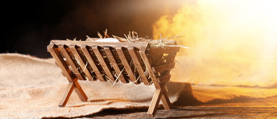 Manger with baby Jesus and cloth on table against dark background