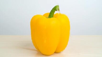 A vibrant yellow bell pepper with a green stem is being splashed with water against a white backdrop - Powered by Adobe