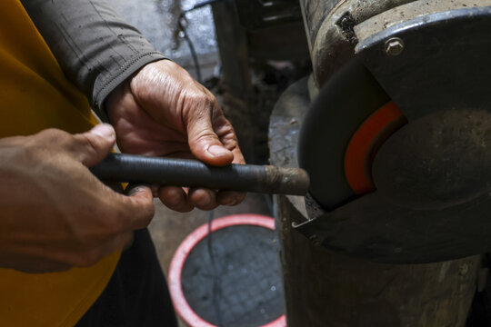 Focused worker hands sharpening metal tool on grinding machine in workshop. Close up of craftsman at work, using grinder for precision and skill in manufacturing