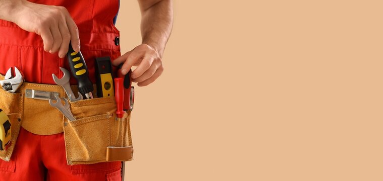 Male worker wearing tools belt on beige background with space for text, closeup