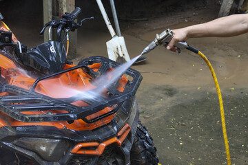 Focused person using pressure washer for cleaning muddy orange all terrain vehicle in garage. High pressure water jet spraying for quad bike maintenance and care © CoreRock