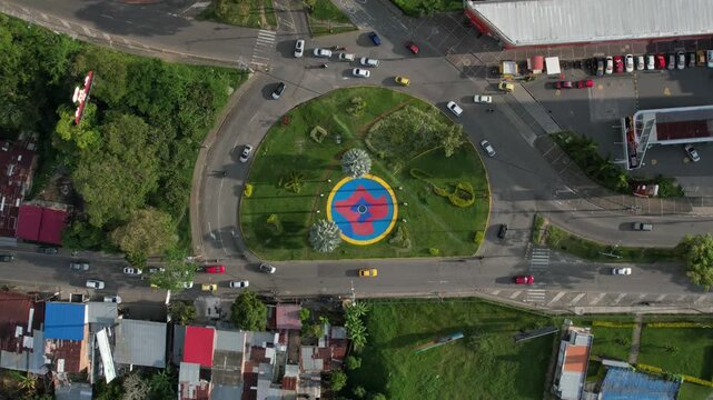 Dynamic aerial hyperlapse of traffic moving through the Milla de Oro roundabout in Ibagu&eacute;, Colombia, showing urban life, busy roads, and surrounding green spaces from above.