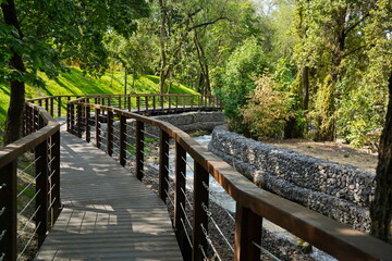 A wooden bridge with a fence along the river. Park area.  Terrenkur.