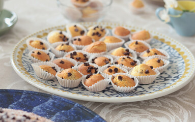 Mini chocolate cupcakes on patterned ceramic plate. Holidays and lifestyle. Food on table covered with tablecloth. 