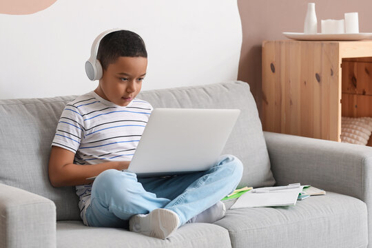 Little African-American boy in headphones with laptop studying computer sciences online at home - Powered by Adobe
