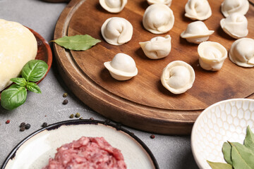 Wooden board with uncooked dumplings on grey background