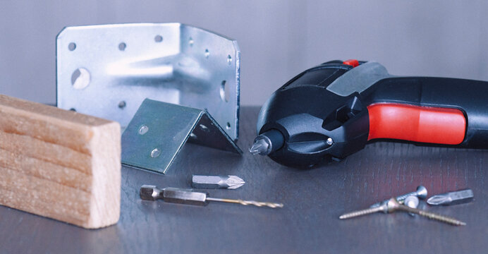 Tools and hardware arranged for construction work on a wooden surface with metal brackets and screws present