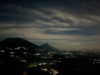Night mountain landscape with sparkling city lights under a cloudy sky