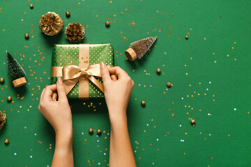 Female hands with Christmas gift box and pine cones on green background