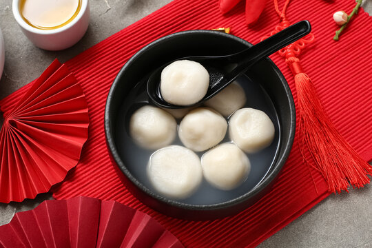 Red mat with bowl of tangyuan and Chinese decor on grey grunge background, closeup. Dongzhi Festival