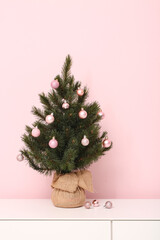 Dresser with small Christmas tree near pink wall