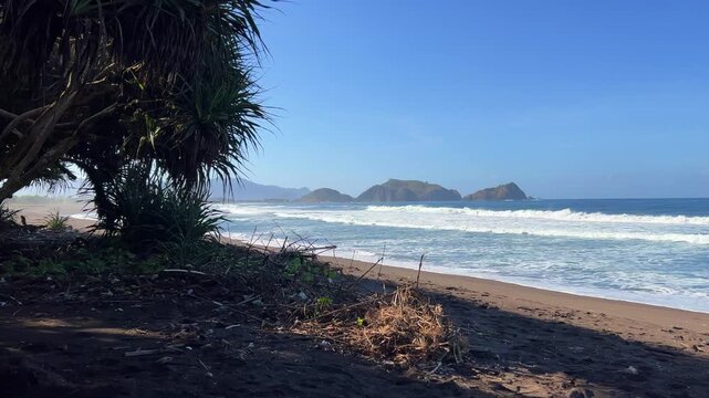 The sea in Jember, East Java. Indonesia. Watu Ulo beach with dark sand, mountains and coral rocks towering above the beach. The raging blue Indian ocean on a sunny day. 4К