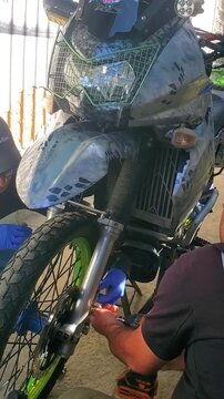 Vertical video DIY motorcycle Project. Men working on custom dual-sport motorcycle featuring camouflage paint, detail suspension system