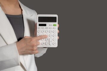 Businesswoman in suit holding calculator on grey background