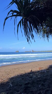 The sea in Jember, East Java. Indonesia. Watu Ulo beach with dark sand, mountains and coral rocks towering above the beach. The raging blue Indian ocean on a sunny day. 4К