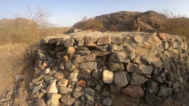 Close-up, atmospheric shot of a circular dry-stone well structure in rocky desert hills with distant mountains under a bright sky &mdash; ideal stock B-roll for landmarks, travel, archaeology projects.